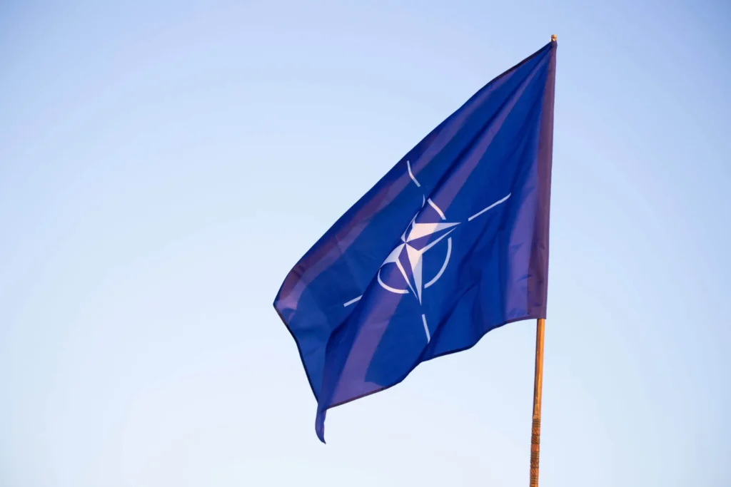 Vlajka NATO vejúca na stožiari proti modrej oblohe