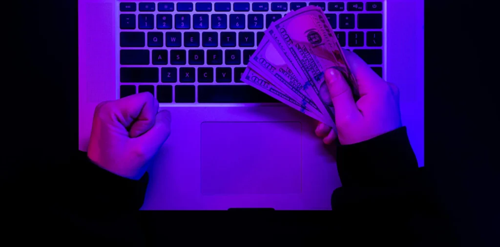 Ruky držiace hotovosť nad klávesnicou laptopa – ilustrácia finančných škôd spôsobených ransomwarom